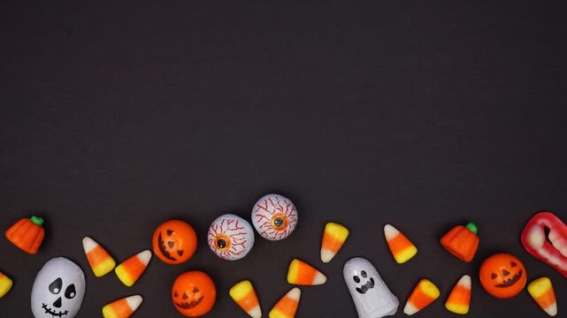 Halloween bottom border of a variety of candy. Top view stop motion loop video over a dark black background with copy space.
