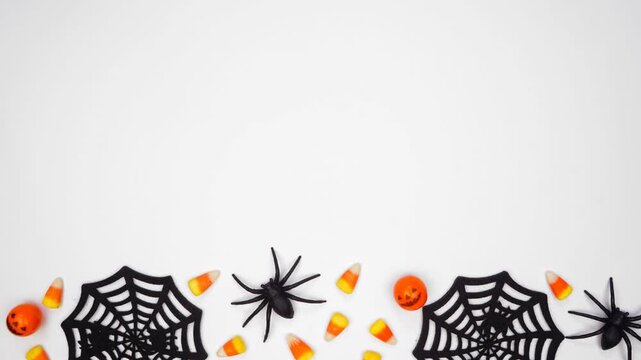 Halloween bottom border of scattered candy and spider webs. Above view stop motion loop video over a white background with copy space.