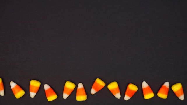 Halloween candy corn bottom border. Above view stop motion loop video over a dark black background with copy space.