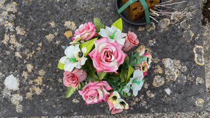 Bouquet of artificial flowers on an old tombstone covered with lichen