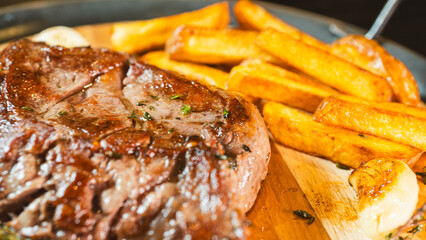 Perfectly cooked medium rare ribeye steak, juicy, on a wooden board with homemade cut fries, fresh thyme, and roasted garlic. Top view food photography for menus and recipes.