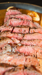 Juicy sliced medium rare ribeye steak served on a wooden board with roasted garlic, fresh thyme,...