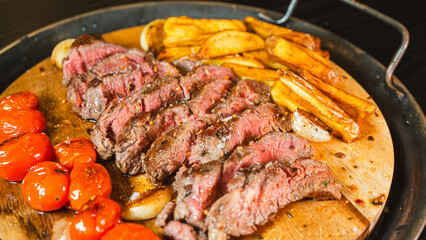 Juicy sliced medium rare ribeye steak served on a wooden board with crispy homemade fries, roasted garlic, fresh thyme, and cherry tomatoes. Perfect for food blogs and menus.