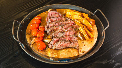 Juicy sliced medium rare ribeye steak served on a wooden board with crispy homemade fries, roasted garlic, fresh thyme, and cherry tomatoes. Perfect for food blogs and menus.