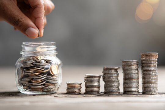Saving money with coins in a jar and stacked coins on a table.