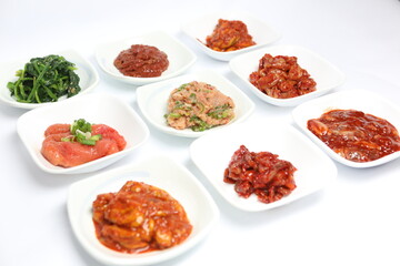 High resolution photo of assorted Korean jeotgal (fermented seafood side dishes) served in small white bowls on white background. A traditional Korean cuisine and popular banchan.