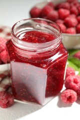 Delicious raspberry jam in glass jar and fresh berries on white table, closeup