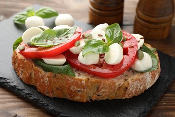 Delicious sandwich with mozzarella cheese, tomatoes and basil on wooden table, closeup