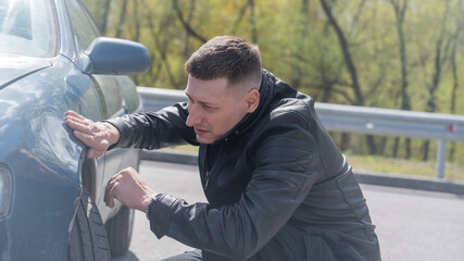 A Caucasian man inspects damage to his car. 