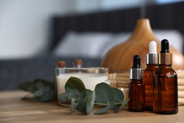 Spa composition with aroma oil diffuser and burning candles on wooden table, closeup