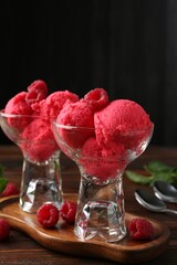 Delicious raspberry sorbet in dessert bowls, mint and fresh berries on wooden table against black background, closeup