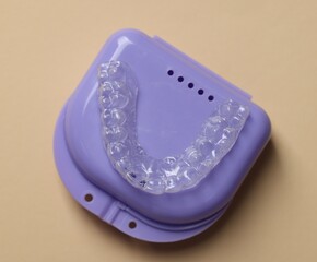 Clear aligner in retainer case on beige background, top view