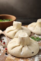 Uncooked khinkalis (dumplings) with spices on wooden board, closeup