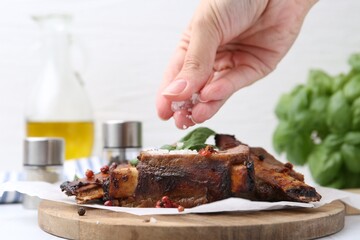 Woman salting roasted beef ribs at table, closeup