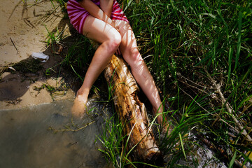 Child Dangling Feet in Stream on Weathered Log