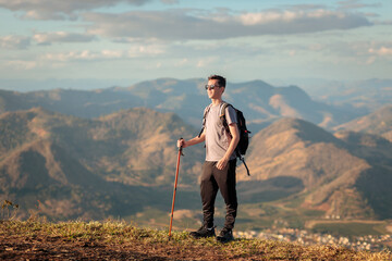 Traveler standing with trekking pole and backpack, admiring the scenic mountain view on a sunny day...