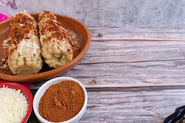A plate with a pair of cooked and prepared corn on the cob, along with chili powder and grated cheese, Mexican food