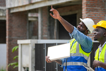Two professional Black engineers collaborating on a building project. A skilled architect discusses...