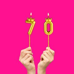 Birthday on a fuchsia background with the number 70 - Hands holding number-shaped candles
