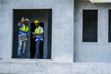 Engineers on a construction site inspect a solar panel, discussing its placement on the building's...