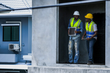 An experienced construction foreman mentors a young apprentice on a building site. The senior engineer uses a tablet to explain project details, providing on-the-job training and guidance.