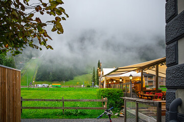 An illuminated hillside cafe at the base of Mt Titlis in the town of Engelberg, Switzerland, Swiss Alps, with a mountain funicular behind as fog rolls in.