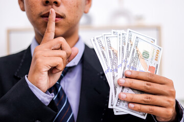 Man in a Suit Holds Cash and Puts Finger To Lips Signaling Secrecy