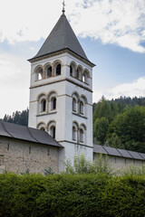 bell tower of Putna Monastery in Romania, with its distinct arched windows and solid structure, stands prominently against a dramatic sky. 
