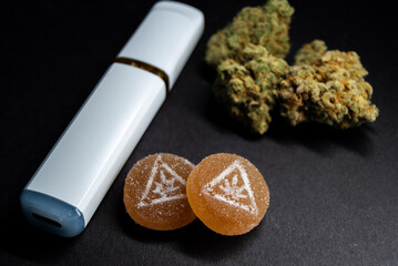 Close up macro shot of marijuana gummies, vape, and buds on black background