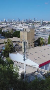 Telephone tower monopole antenna is hiding behind trees next to a factory in a modern industrial area - Vertical video