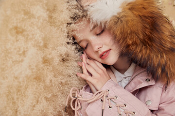 Teen girl in pink fur-lined coat resting against soft background.