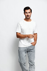Full body smiling young man wearing white t-shirt and grey pants, looking at the camera while...