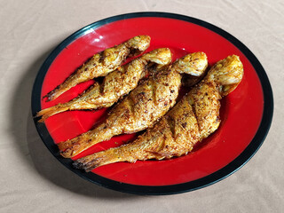 Four crispy, golden fried fish served on a red plate with black lines.