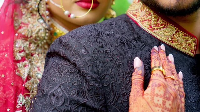 Bride holding the groom. Traditional henna painted bridal hand. Red and black colors in the Indian embroidered clothes, Elements of Asian wedding. 