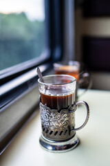 Close up tea in glass with metal holder and spoon on train table near window. Travel drink, railway tea, onboard beverage, warm drink journey, classic train service, retro long distance comfort