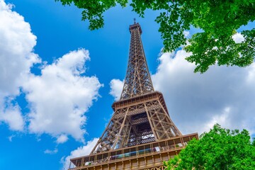 Capture the Eiffel Tower from a unique angle, framed by vibrant greenery and a bright blue sky with fluffy clouds. This image epitomizes the beauty of Paris and its allure for travelers.