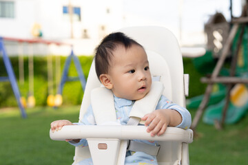 A 10-month-old baby sits in a stroller and enjoys nature at a park in the warm morning sunlight.