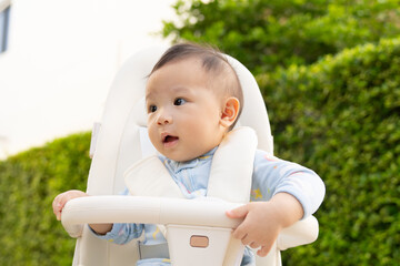 A 10-month-old baby sits in a stroller and enjoys nature at a park in the warm morning sunlight.