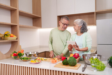Asian older couple cooking healthy food preparing vegetables using tablet recipe guidance modern kitchen home environment