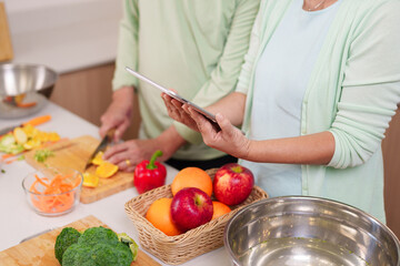 Older Asian couple prepare healthy meals home kitchen digital tablet recipe guidance fresh vegetables and fruits cooking instruction