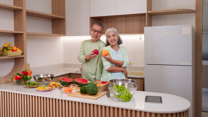Asian senior couple prepare healthy meal in modern kitchen enjoying vibrant fresh fruits vegetables...