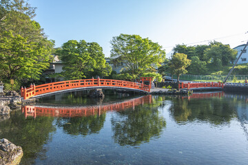Red wooden bridge over pond in peaceful Japanese garden with green trees at Fujinomiya, Shizuoka,...