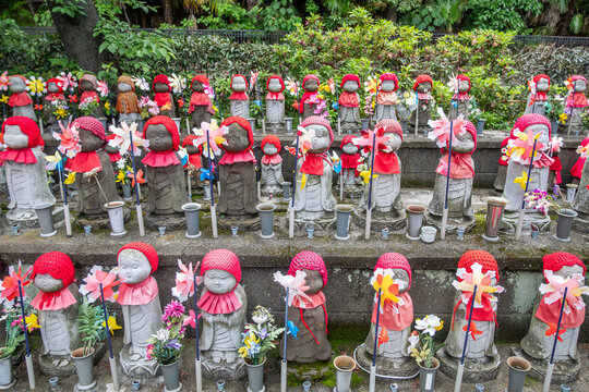 Jizo statues wearing red hats and bibs at Japanese temple garden with flowers at Tokyo, Japan