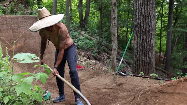Man building BMX MTB dirt jumps in forest packing dirt - slow motion