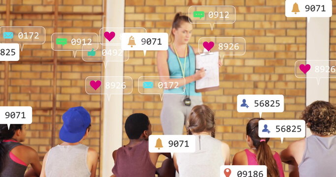 Holding clipboard stopwatch, coach in leggings tank top guiding trainees in gym, social media icons