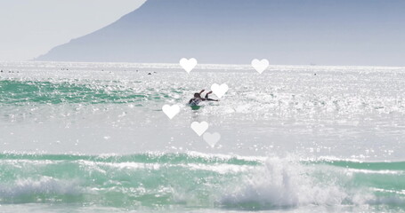 Obraz premium Gliding female surfer paddling on surfboard in ocean surf zone, with wetsuit and sparkling waves
