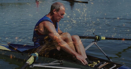 Adjusting foot straps senior rower wearing blue top leaning in scull on calm river, with oars