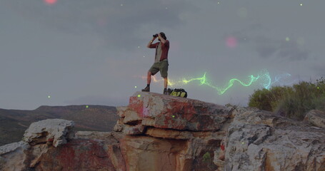 Scanning hiker wearing wide-brimmed hat on cliff with binoculars, backpack and neon trails