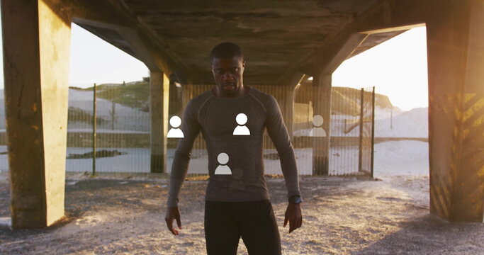 Standing African American man training under concrete pillars on beach at sunset, with smartwatch