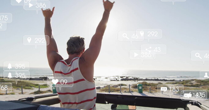 Raising arms mature male celebrating in open-top convertible on coastal path, with social icons